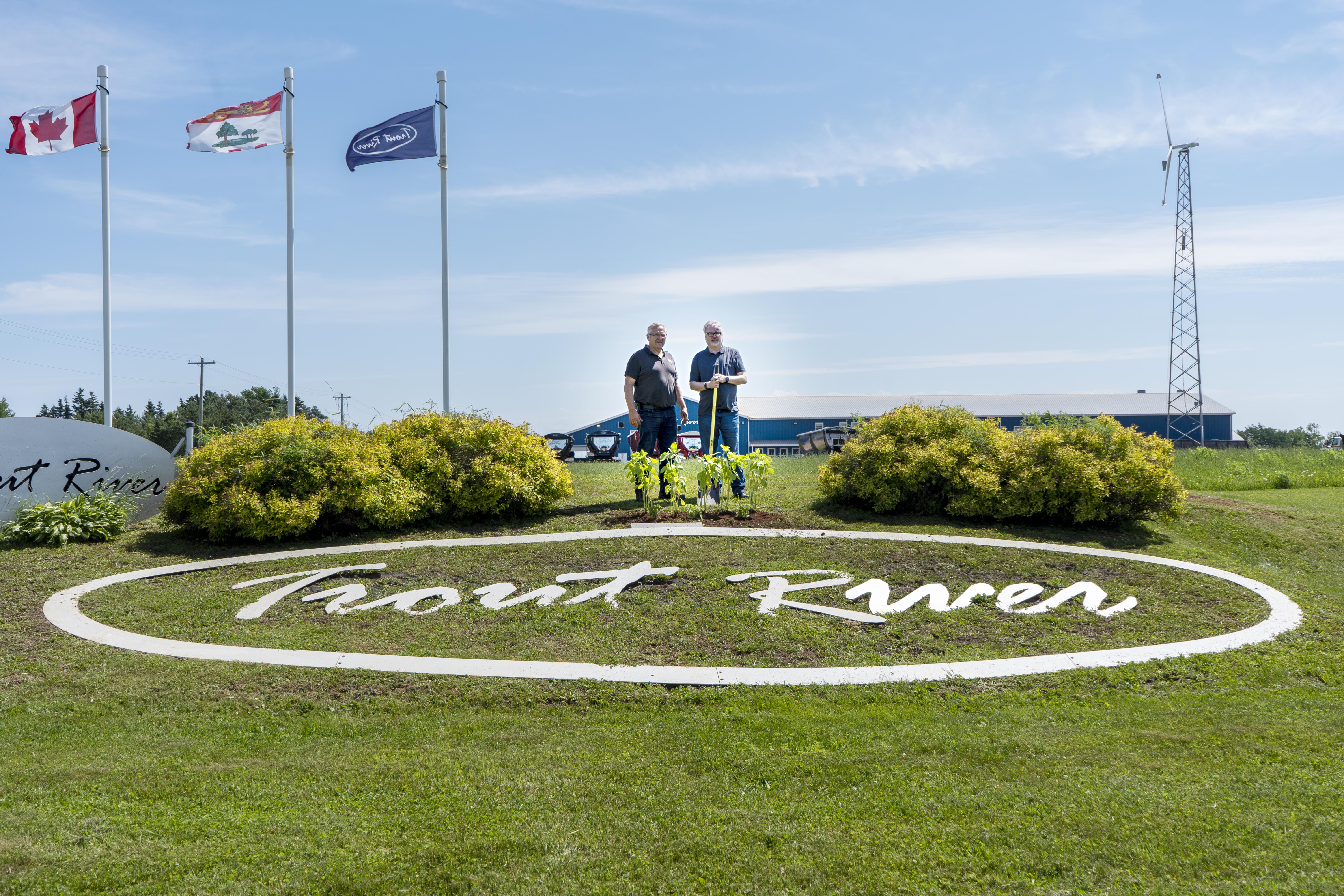 2 People Standing behind the Trout River Logo on the grass
